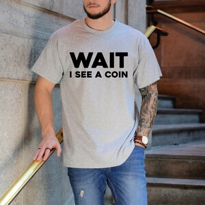 May include: A gray t-shirt with the text "WAIT I SEE A COIN" printed in black.