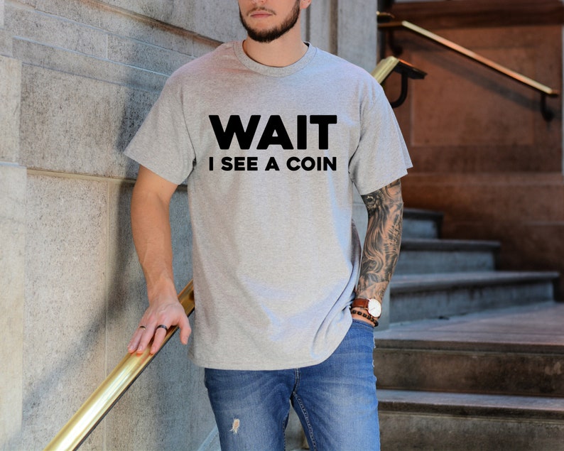 May include: A gray t-shirt with the text "WAIT I SEE A COIN" printed in black.