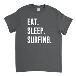 Puede incluir: Una camiseta gris oscuro con texto blanco que dice "EAT. SLEEP. SURFING."