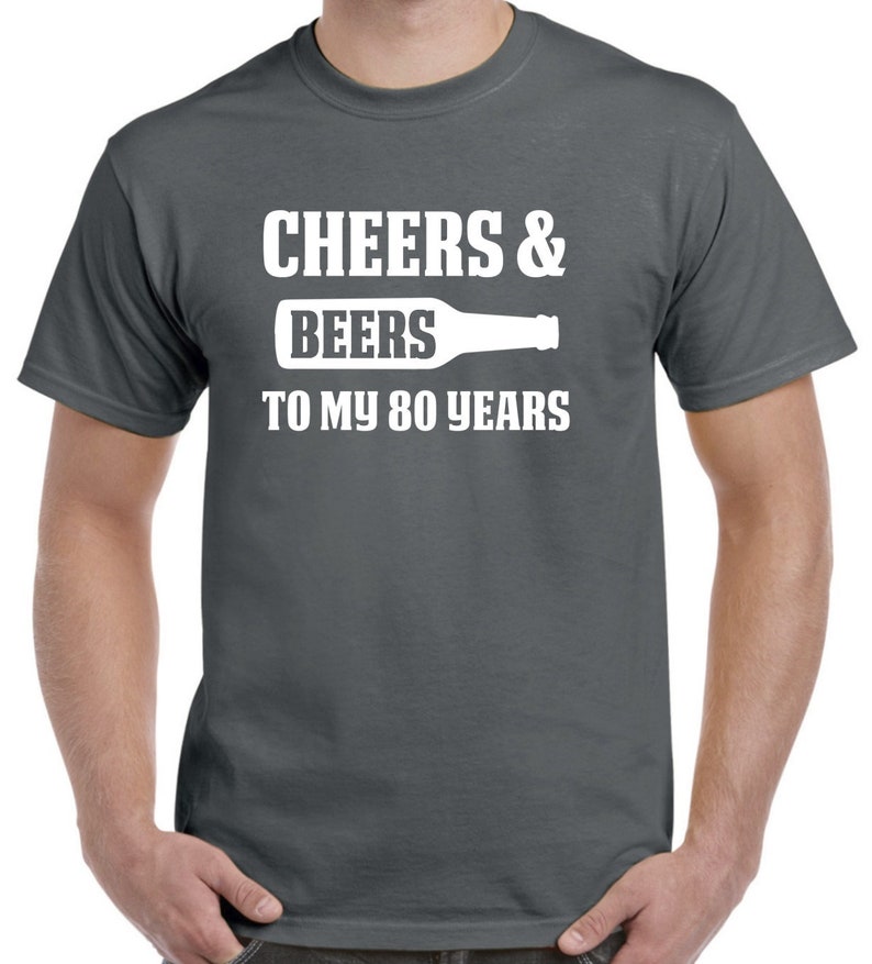 Puede incluir: Una camiseta gris oscuro con texto blanco que dice "Cheers & Beers to my 80 years" y una silueta de una botella de cerveza.