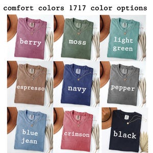 K&ouml;nnte beinhalten: Ein Raster aus neun Comfort Colors 1717 T-Shirts in den Farben Berry, Moss, Light Green, Espresso, Navy, Pepper, Blue Jean, Crimson und Black. Jedes T-Shirt hat einen Rundhalsausschnitt, ein sichtbares Markenetikett und wei&szlig;en Text.