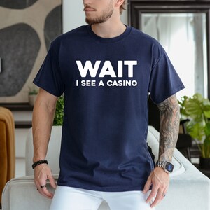 Pu&ograve; includere: Una t-shirt blu navy con testo bianco che recita "WAIT I SEE A CASINO".
