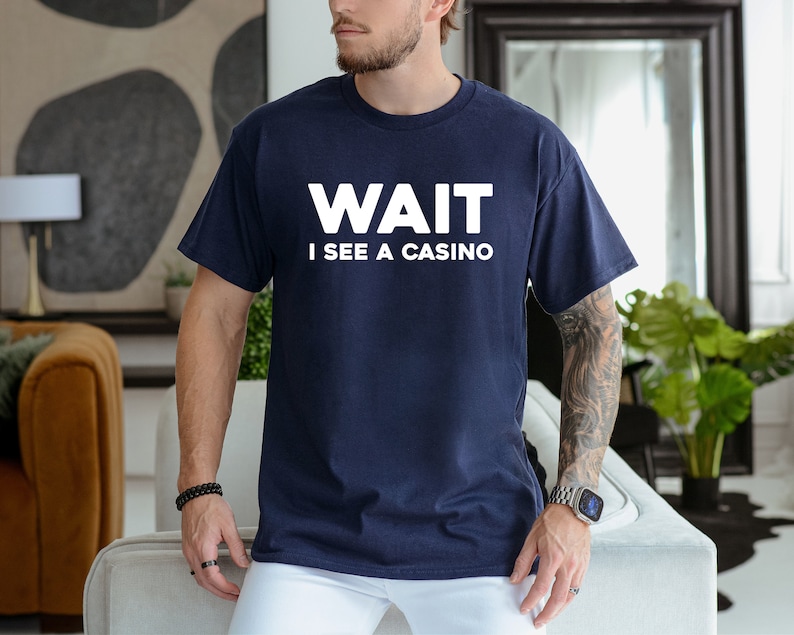 Pu&ograve; includere: Una t-shirt blu navy con testo bianco che recita "WAIT I SEE A CASINO".