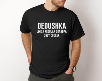Puede incluir: Camiseta negra con el texto blanco "DEDUSHKA LIKE A REGULAR GRANDPA ONLY COOLER." La camiseta es de cuello redondo y la lleva una persona.