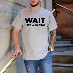 Pu&ograve; includere: Una maglietta grigia con testo nero che dice "WAIT I SEE A CASINO".