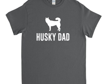 May include: A dark gray t-shirt with a white silhouette of a husky dog and the text "HUSKY DAD" printed on the front.