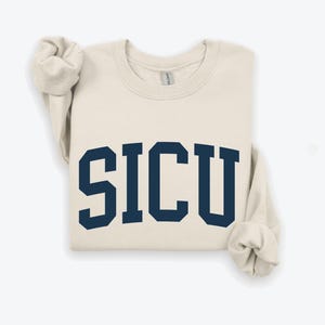 May include: A cream colored sweatshirt with the word "SICU" printed in navy blue.