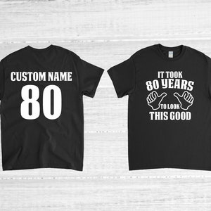 May include: Two black t-shirts. One shirt has the text "CUSTOM NAME 80" on the back. The other shirt has the text "IT TOOK 80 YEARS TO LOOK THIS GOOD" with two thumbs up on the front.