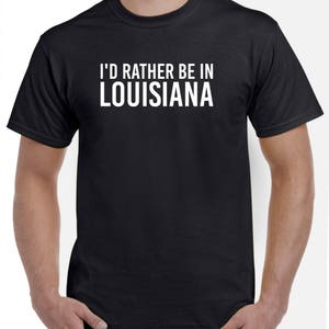 May include: Black t-shirt with white text that reads "I'd rather be in Louisiana".