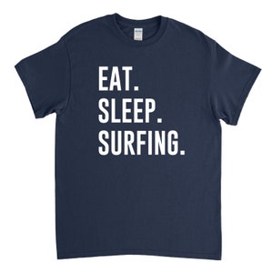 Puede incluir: Una camiseta azul marino con texto blanco que dice "EAT. SLEEP. SURFING."