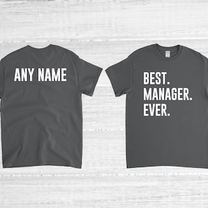 May include: Two dark gray t-shirts with white text. The front of one shirt says "BEST. MANAGER. EVER." The back of the other shirt says "ANY NAME".