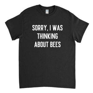 以下が含まれることがあります： 黒いTシャツに白い文字で「ごめんなさい、ハチの事を考えていました。」と書いてあります