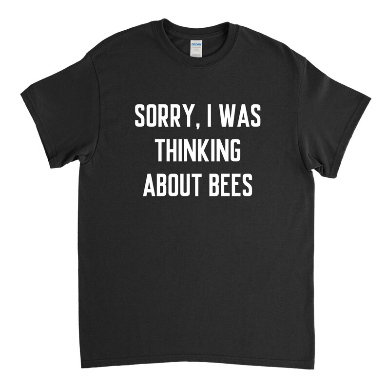 以下が含まれることがあります： 黒いTシャツに白い文字で「ごめんなさい、ハチの事を考えていました。」と書いてあります