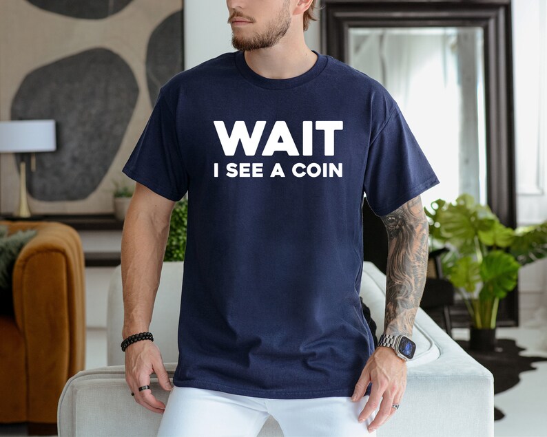 May include: A navy blue t-shirt with white text that reads "WAIT I SEE A COIN".