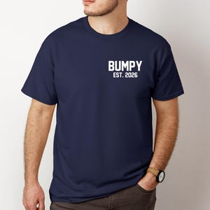 May include: Navy blue t-shirt with the word "BUMPY" and the text "EST. 2026" printed in white. The shirt is a crew neck style and has short sleeves. The text is centered on the upper chest.
