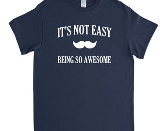 May include: A navy blue t-shirt with white text that reads "It's not easy being so awesome" and a white mustache graphic.