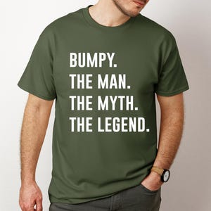 May include: Olive green t-shirt with the text "BUMPY. THE MAN. THE MYTH. THE LEGEND." in white. The shirt is a crew neck style and is being worn by a person.