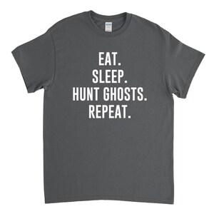 May include: A dark gray t-shirt with white text that reads "Eat. Sleep. Hunt Ghosts. Repeat."
