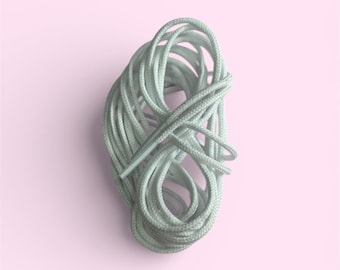 May include: A bundle of light green shoelaces, tightly coiled, against a soft pink background. The laces are a solid color, with a smooth texture. The image is a top-down view, highlighting the laces' form and color.