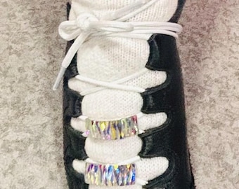 May include: Close-up of a black and white Irish dance shoe with white laces and a white sock. The shoe has two rows of iridescent rhinestones. The sock is white with silver embellishments.