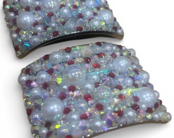 May include: Two decorative hair clips, each adorned with a mix of white pearls, red beads, and iridescent crystals. The clips have a curved shape and a dark base, creating a sparkling, elegant accessory.