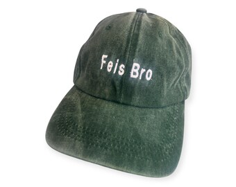 May include: A dark green baseball cap with the embroidered text "Feis Bro" in white. The cap has a curved brim and a small, rounded button on top. The fabric appears to be slightly faded, giving it a vintage look.