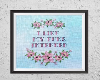 May include: A framed cross-stitch with a light blue background and pink flowers. The text reads "I like my puns intended".