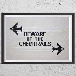 May include: A black and white cross-stitch design in a black frame. The design features two airplanes leaving trails and the text "BEWARE OF THE CHEMTRAILS".