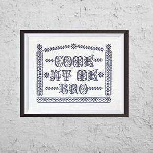 May include: A framed cross-stitch design with a white background and black embroidery. The design features the text "COME AT ME BRO" in a decorative font.