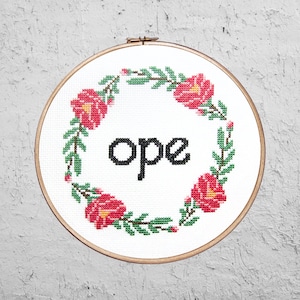 Peut inclure: Art de broderie sur un cercle avec un fond blanc et une couronne de fleurs rouges et de feuilles vertes. Le mot "ope" est brodé en noir au centre du cercle.