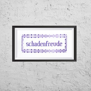 May include: A framed cross-stitch with a purple and white design. The cross-stitch says "schadenfreude" in a purple font.