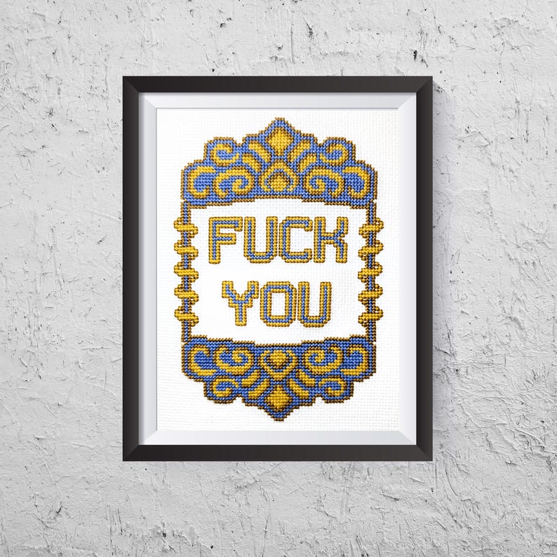 May include: Framed cross-stitch art with the words "FUCK YOU" in yellow, centered on a white background. The text is framed by a blue and gold decorative border. The artwork is in a black frame.