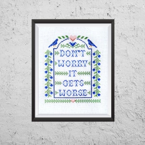 Peut inclure: Broderie au point de croix encadrée avec le texte « DON'T WORRY IT GETS WORSE ». Le motif comprend des oiseaux bleus, des fleurs et un cœur, le tout en bleu et vert. Le fond est blanc, et le cadre est noir.
