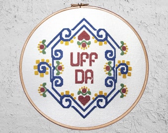 Pode incluir: Um aro de bordado branco com um design geométrico azul, vermelho e amarelo. As palavras "UFF DA" são bordadas em letras vermelhas no centro do design.