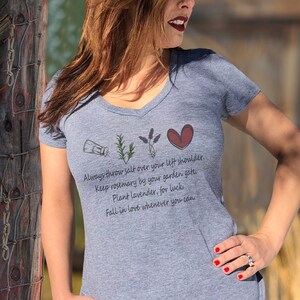 May include: Gray V-neck t-shirt with a graphic of a salt shaker, rosemary, lavender, and a heart. The text on the shirt reads: "Always throw salt over your left shoulder. Keep rosemary by your garden gate. Plant lavender, for luck. Fall in love whenever you can."