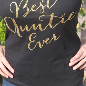 May include: Black v-neck t-shirt with gold glitter lettering that reads "Best Auntie Ever".