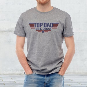May include: A gray t-shirt with a blue and red graphic that says "Top Dad Est. 2022" with a star underneath.