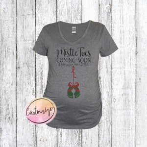 May include: Gray V-neck maternity shirt with the text "Mistle Toes Coming Soon" and "Baby Jackson March 2022". The shirt features a green and red illustration of a baby's feet with a red bow.