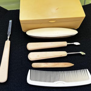 Könnte beinhalten: Ein Set Maniküre-Werkzeuge in einer Holzkiste. Das Set enthält eine Nagelfeile, einen Nagelhaut-Schieber, eine Pinzette und einen Kamm. Die Werkzeuge sind alle aus Metall und haben Holzgriffe.