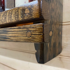 May include: A two-tiered wooden shelf with a dark brown stain. The shelf is made from reclaimed wood and has a rustic look. The shelf is mounted to a wall and has a small lip on the front edge to prevent items from falling off.