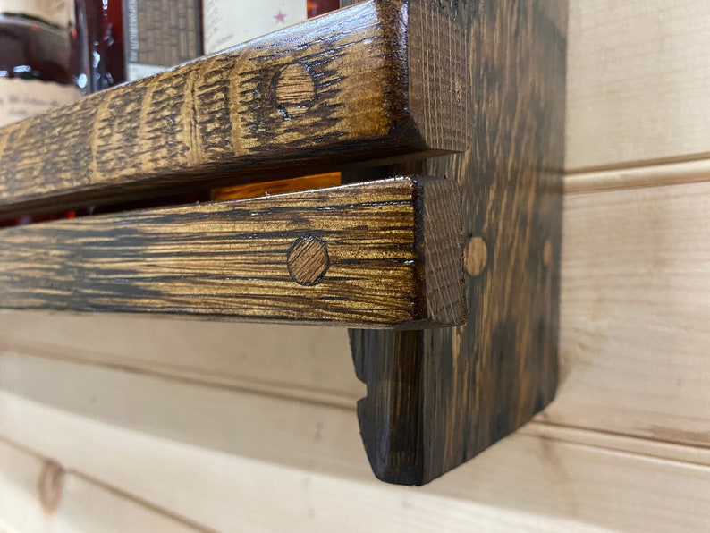 May include: A two-tiered wooden shelf with a dark brown stain. The shelf is made from reclaimed wood and has a rustic look. The shelf is mounted to a wall and has a small lip on the front edge to prevent items from falling off.