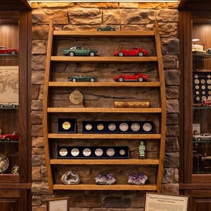 May include: A wooden wall-mounted display shelf with six tiers, holding various die-cast model cars, a brass astrolabe, a book, two coin display cases, a small figurine, and three mineral specimens, all set against a textured stone wall background.