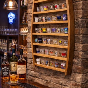 May include: A wall-mounted wooden display rack crafted from a curved barrel stave, featuring six horizontal shelves holding a collection of various small glass shot glasses with colorful designs and patterns arranged in rows.