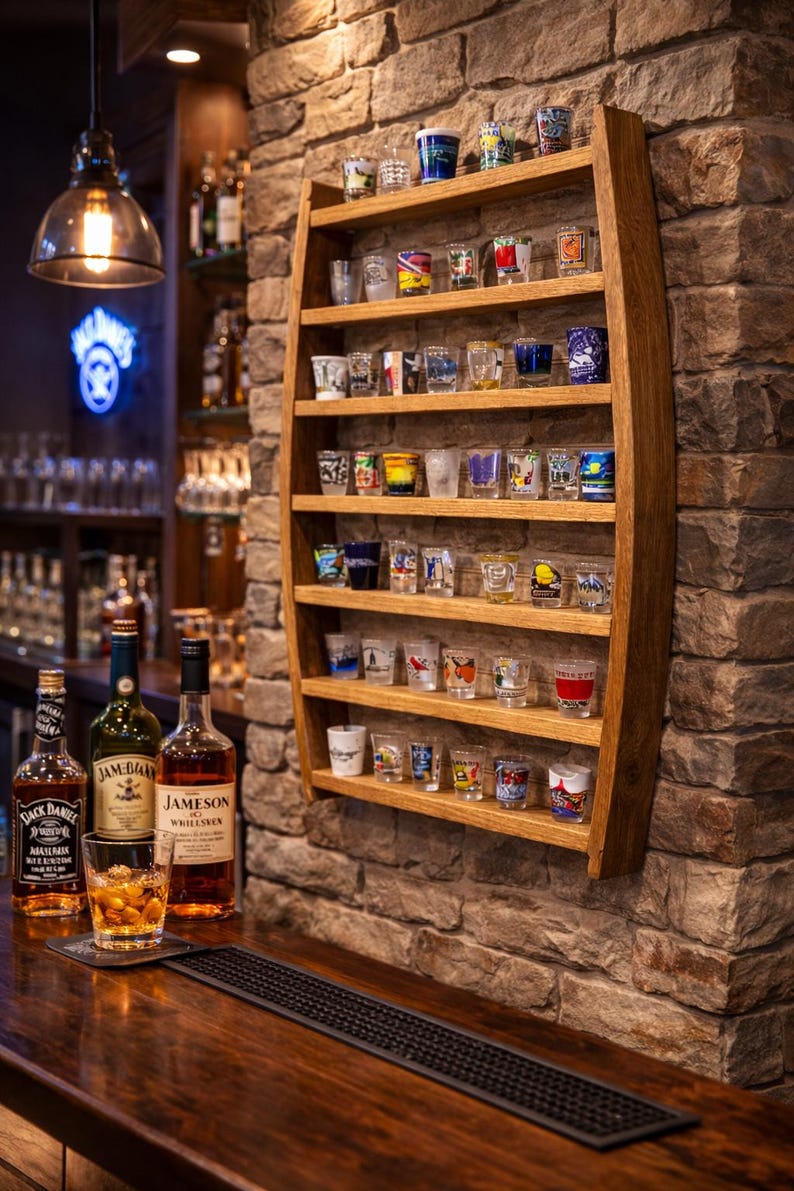 May include: A wall-mounted wooden display rack crafted from a curved barrel stave, featuring six horizontal shelves holding a collection of various small glass shot glasses with colorful designs and patterns arranged in rows.