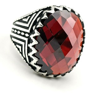 May include: A silver ring with a large, faceted, red gemstone. The ring has a detailed, geometric design on the band.