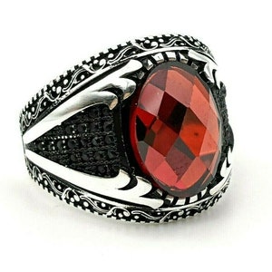 May include: A silver ring with an ornate design and a large red gemstone.