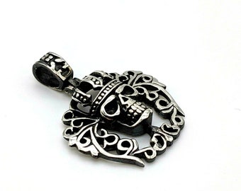 May include: Silver pendant featuring a skull wearing a crown, surrounded by ornate scrollwork.
