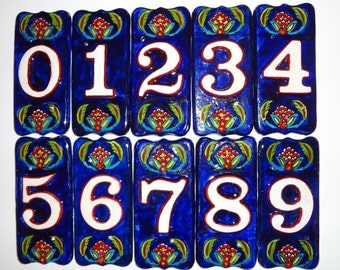 Puede incluir: Diez azulejos de cerámica con fondo azul y números blancos del 0 al 9. Cada azulejo tiene un diseño floral en rojo, amarillo y verde.
