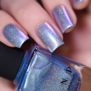 May include: A bottle of light blue nail polish with a holographic finish. The bottle is labelled "ILNP" and "que nail lacquer". The bottle contains 0.4 fl oz.
