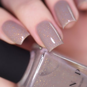 May include: A close-up of a bottle of light brown nail polish with gold glitter. The bottle is labeled "ND" and has a black cap. The polish is shown on a person's fingernails.